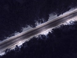 Night time aerial top down view of a snowy road surrounded pine tree forest in winter season.