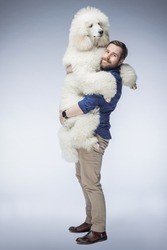 happy white guy holds a white poodle puppy in his arms. A man smiles at his dog in the isolated background. The dog and its owner.