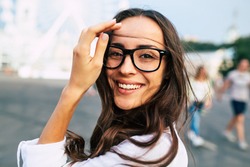 Beautiful happy young woman in glasses having good time on city square while walking outdoors