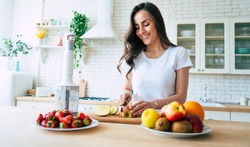 Beautiful woman making fruits smoothies with blender. Healthy eating lifestyle concept portrait of beautiful young woman preparing drink with bananas, strawberry and kiwi at home in kitchen.