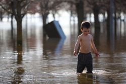 Young toddler plays in water of flooded park after heavy rain storm