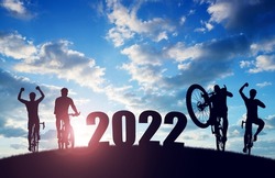 Silhouette of cyclists with bicycles at sunset. Forward to the New Year 2022. Holiday concept.