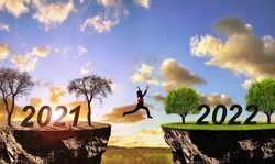 Girl jumping from arid land with number 2021 on lush landscape with number 2022. Concept of Happy New Year. Global warming or change climate theme.