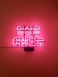 Korean neon sign stationary on the wall.
'Everyday as a trip.' 
