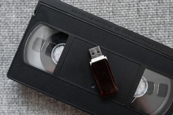 Old tape video cassette with usb flash disk on gray knitted background