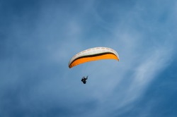 Man on a paraglider flying high in blue sky.