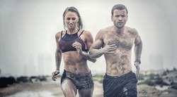 Muscular male and female athlete covered in mud running down a rough terrain with a desert background in an extreme sport race with grungy textured finish