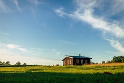 Small house in rural field, view on small cottage house in countryside, summer evening.