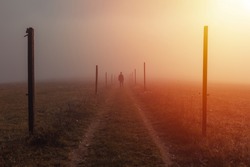 Silhouette young man walk on path with wooden stick in misty fog at sunrise, Czech landscape