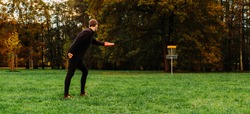 Young caucasian man playing disc golf on autumn play course with basket