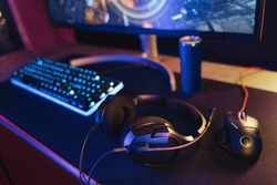 View of pro gaming desk setup with headset, keyboard, monitor and computer mouse illuminated by neon lights. Cyber sport equipment laying on desktop, ready for online video shooter games and streaming