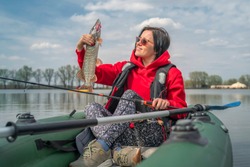 Kayak fishing. Fisher girl holding pike fish trophy on inflatable boat with fishing tackle at lake.