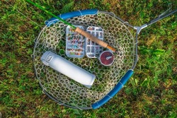 Fly fishing tackle. Tackle box with flies, rod, reel and thermo water bottle on fishing landing net.