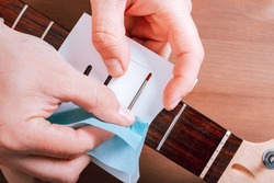 Guitar master polishing frets of electric guitar with template on wooden table top with guitar care instruments around