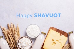 Shavuot flat lay with dairy products and wheat on light gray background, Happy Shavuot text. Jewish Shavuot holiday frame with dairy foods and quote happy Shavuot, top view