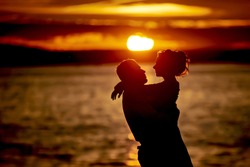 silhouettes in love romantic couple lovers hugging, kissing, touching, eye contact at sunset, sunrise on the background of the sea, the sun, the clouds in fiery red, orange colors