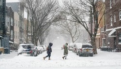 Friends trek through a snow covered street in Brooklyn during a blizzard. 