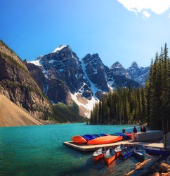 Canoes on a jetty at Moraine lake in Banff National Park, Alberta, Canada, with snow-covered peaks of canadian Rocky Mountains in the background.