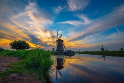 Sunset above historic windmills and a river flowing by in Kinderdijk, Netherlands. This system of 19 windmills was built around 1740 and is a UNESCO heritage site.