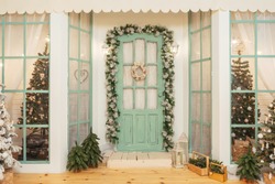 Porch with green door in Christmas decorations and Christmas trees. Spruce garlands around the door. Beautiful winter terrace of the house with garlands of retro light bulbs