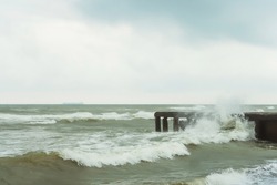 The base of an old concrete pier in the Black Sea. The stone base of the pier in the waves and foam in the ocean in cloudy weather. Destroyed pier on the beach in Magnetiti Ureki in Georgia
