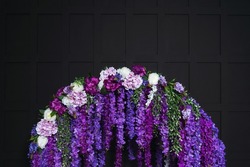 purple flowers on a black background. artificial flowers on an arch on a dark background in a photo studio. detail of the wedding photo zone in the photo studio