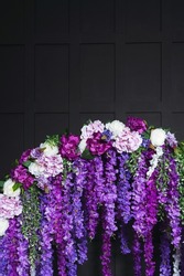 purple flowers on a black background. artificial flowers on an arch on a dark background in a photo studio. detail of the wedding photo zone in the photo studio
