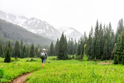 Open valley with man hiker walking in rain on Conundrum Creek Trail in Aspen, Colorado in 2019 summer on cloudy day and dirt road