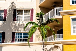 Florida condominium colorful yellow multicolored buildings facade exterior with windows, palm trees, real estate property spanish architecture