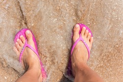 Flat top above view down of brown orange sea sand in Marineland, Florida beach with woman feet pink slippers flip-flops with wave crashing on shore
