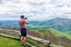 Devil's Knob overlook with man standing photographing taking picture of mountain view by wooden rustic countryside fence at Wintergreen resort town by Virginia Blue Ridge mountains