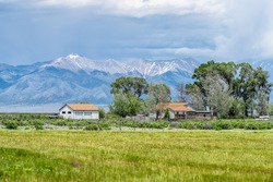 Center, Colorado route road 285 with rural farm pasture and wooden house near Monte Vista and view of Rocky Mountains