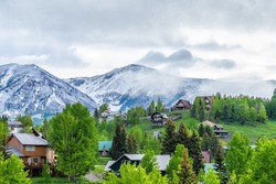 Mt Crested Butte, USA Colorado small village ski resort town in summer with clouds and foggy mist sunrise morning and houses on hills with green trees, mountains in background