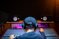 back of asian male professional music producer, sound engineer mixing a song on audio mixing console in recording studio. music production, post production concept