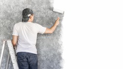 back of young asian man on ladder painting interior cement wall with paint roller for home renovation background