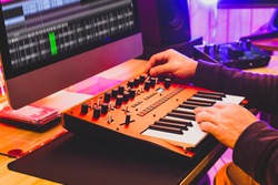 professional sound designer hands playing and tweaking analog synthesizer keyboard knobs for editing sound in post production studio. sound design concept