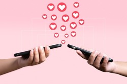 People use mobile phone sending heart to each other. Love and connection concept using telephone application on pink background.