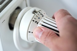 person adjusting thermostat on radiator to lower temperature, saving energy and money concept