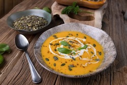 Pumkin soup with fresh cream and pumkin seeds on an old antique wooden table