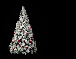 Beautiful decorated christmas tree with a lot of snow on it in front of a black background