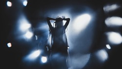 Silhouette of guitar player / guitarist / girl / woman perform on concert stage. Dark background, smoke, concert  spotlights