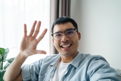 Asian man using smartphone for online video conference call with friends waving hand making hello gesture
