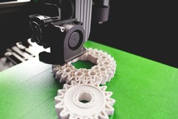 print head, bright green print bed and white helical gears with visible infill and layer. opblique view on process of 3D-printing. copy space for text. selective focus. additive manufacturing concept