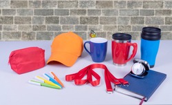 Composition of different promo products with rich colors -Thermo mugs, Lanyards Neck Strap, pens, mug, silver table office clock, zipped coin purse fabric, notebook,cap On desk grey and background gre