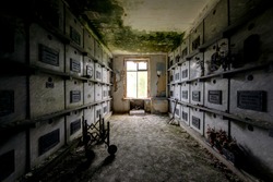 A moody, dark hallway leads to coffins and plaques inside a long abandoned mausoleum.