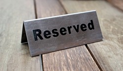 Reserved Table. A tag of reservation placed on the wood table. Reserved logo. Reservation sign. Metal tag with reservation logo. Reserved table in a restaurant. Hungry.