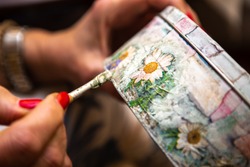 A woman's hand brushing a decoupage on a round jewelry box.