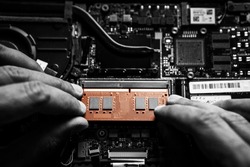 Close-up on the orange RAM memory that the hands of the service technician insert into the slot on the laptop computer.