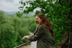 a beautiful woman with red hair blowing in the wind stands in a park overlooking a mountain river. High quality photo
