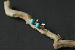 Stud earrings made of natural turquoise sleeping beauty. Designer earrings from natural turquoise stones. Women's jewelry on a black background and wood. Author's modern jewelry.
